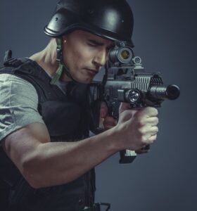 Military recreation player wearing protective helmet aiming pistol ,black armor and machine gun